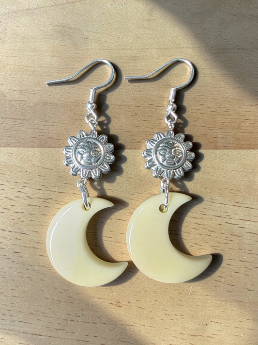 Silver sun and moon earrings on a wooden surface
