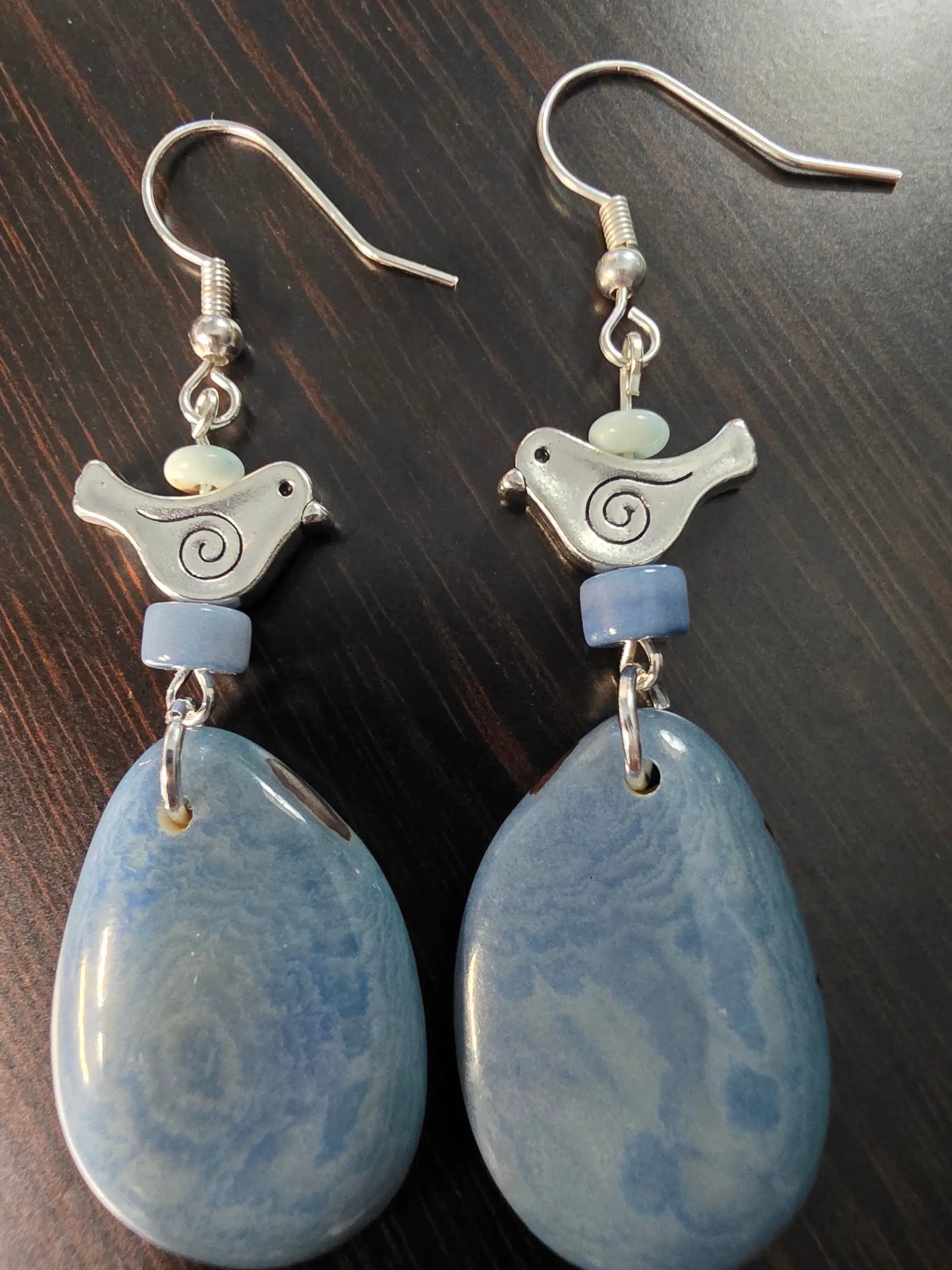 Heather blue tagua grain earrings feature blue ceramic teardrops with silver swirl bird charms and light blue beads
