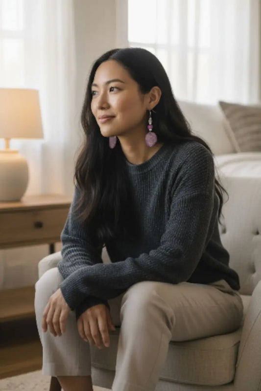 A woman wearing a dark gray knit sweater and beige trousers showcasing lavender swirl engraved tagua earrings with paper beads