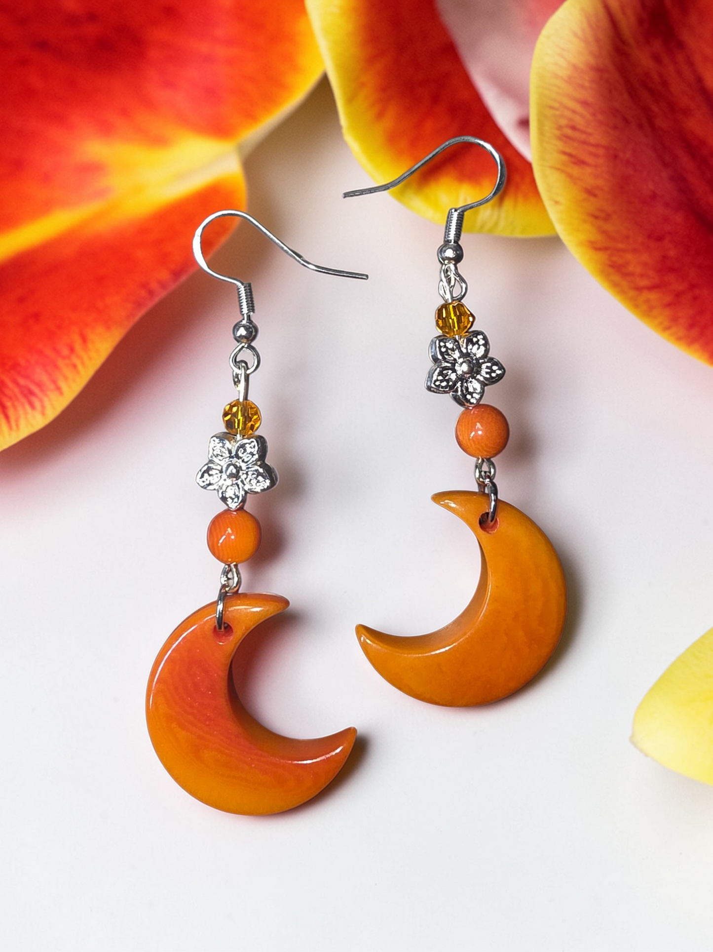 Orange crescent carved tagua moon earrings with floral beads on a white background with orange flowers.