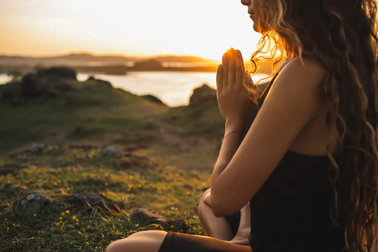 A woman with long wavy hair sits at sunset wearing black to cleanse jewelry energy and clear stagnant energy