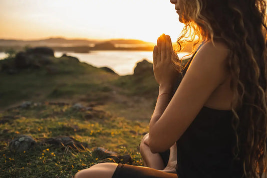A woman with long wavy hair sits outdoors at sunset in a black sleeveless top and dark shorts in a jewelry energy cleansing article