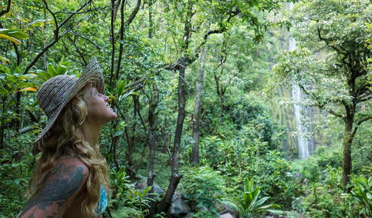 A wide-brimmed natural beige straw hat with woven texture worn by a woman in a lush green rainforest setting