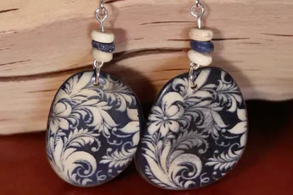 Dark blue oval earrings with intricate white floral patterns silver hooks and stacked cream and navy beads in all earrings collection