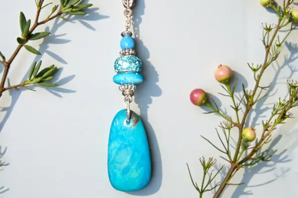A vibrant turquoise pendant necklace with a smooth teardrop stone and decorative silver toned beads from all necklaces collection