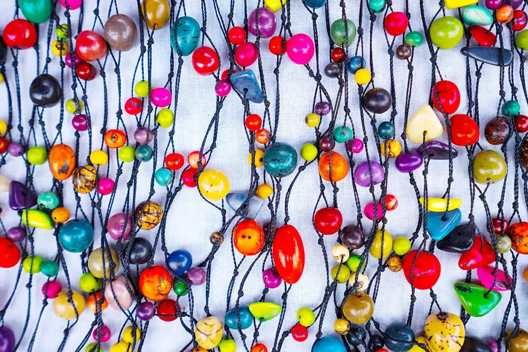 A vibrant collection of colorful handcrafted beads in various shapes strung on black cords from ecuadorian hand-tied traditions