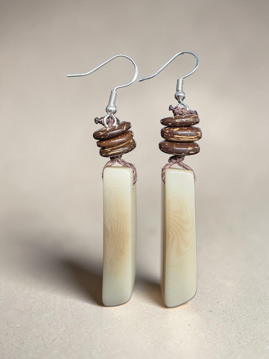 Pair of earrings with cylindrical beige beads and brown spiral accents on a beige background