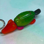 A vibrant hand-carved animal keychain platypus with green body orange head and feet pink underbelly and metallic ring attachment