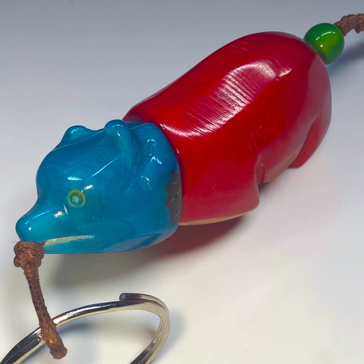 A glossy red and blue hand-carved tagua animal keychain with green bead and braided cord from bear carved rainforest friends