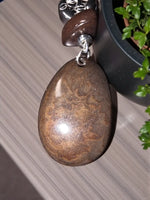 A polished brown sustainable tagua nut necklace with swirling golden patterns on a silver-toned chain