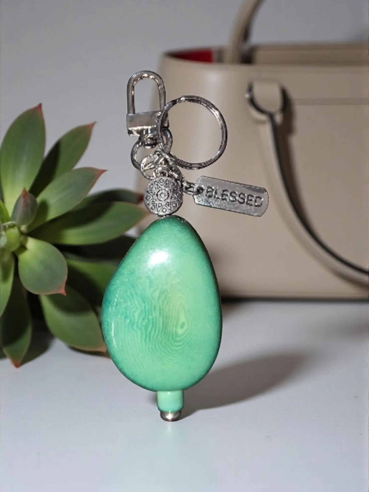 A teal teardrop-shaped large carved turquoise dyed tagua keychain with smooth glossy finish and tibetan amulet bead