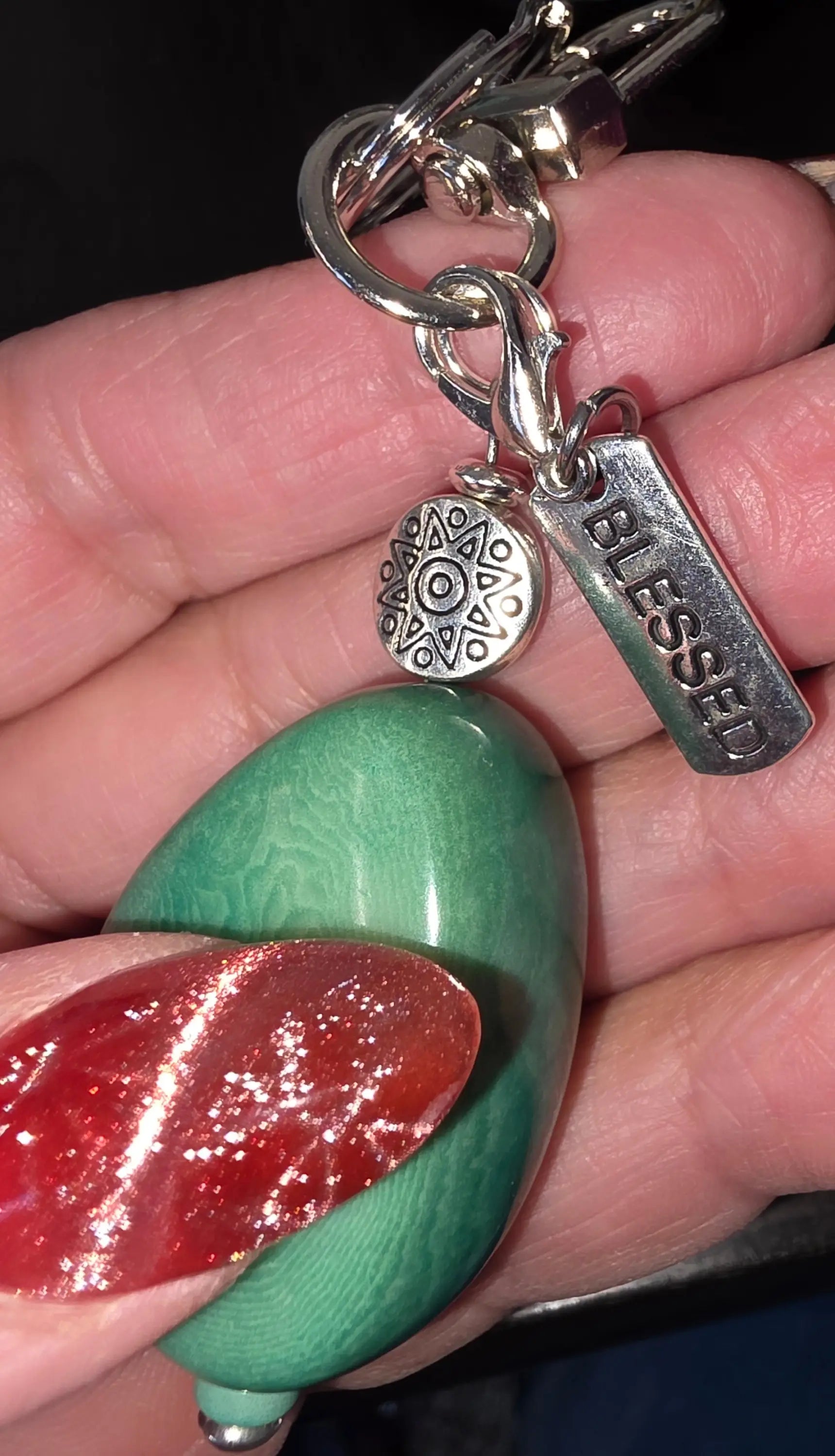 A green oval carved turquoise dyed tagua keychain pendant with a smooth marbled surface and tibetan amulet bead