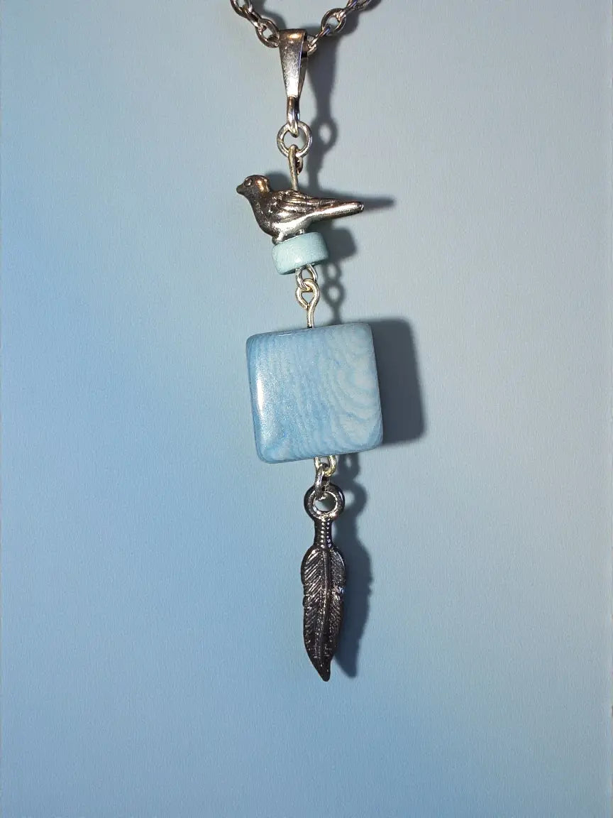 Silver-toned bird charm pendant necklace with light blue square tagua nut bead and dark gray feather accent on chain