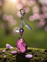 A bag charm featuring a purple natural carved teardrop pendant with brave charm bird amulet and engraved silver tag bergamo