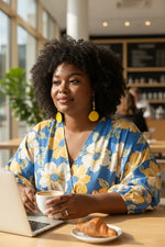 Woman wearing bright yellow tagua nut slice earrings with seahorse bead and blue and yellow floral puffed sleeve blouse
