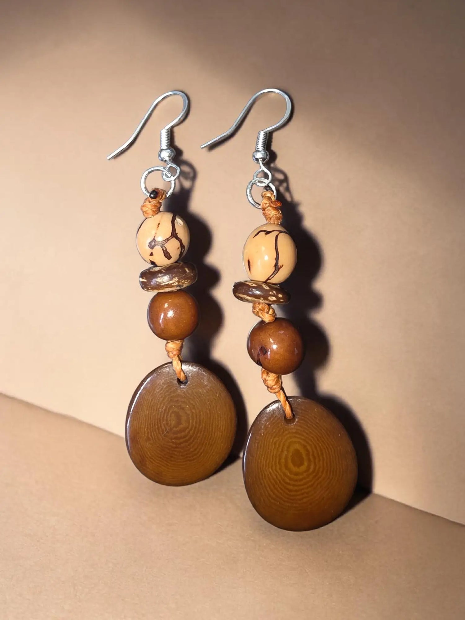 Brown tagua carved vegetable ivory earrings with natural wood grain and silver hooks featuring forest seeds design