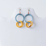 A pair of modern circular tagua earrings with light blue upper hoops and stacked golden-yellow marbled rings