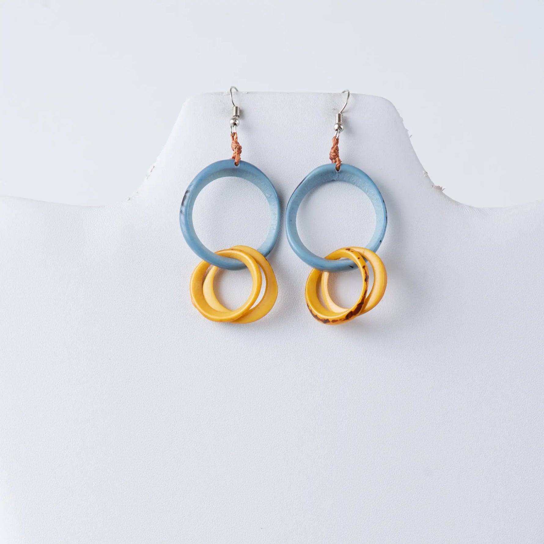 A pair of modern circular tagua earrings with light blue upper hoops and stacked golden-yellow marbled rings