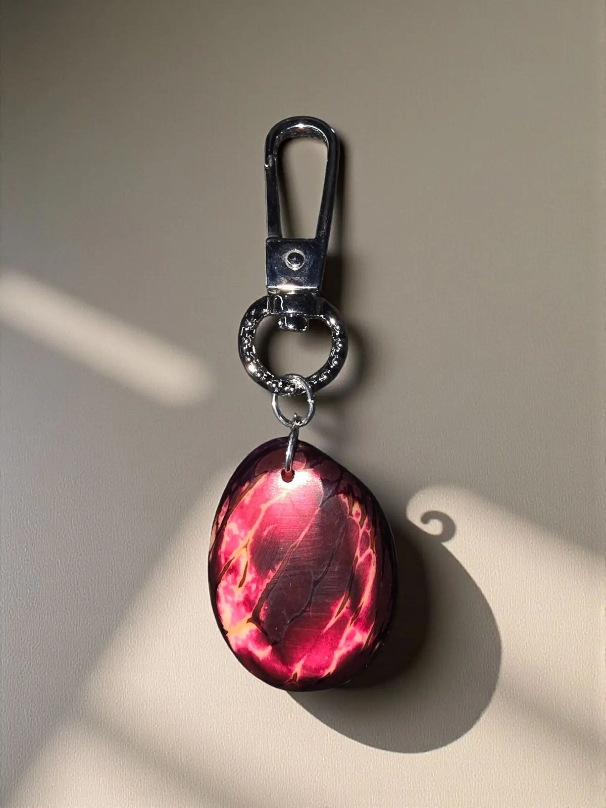 A glossy cobalt blue tagua bag charm with an oval red and pink marbled pendant and silver-toned metal clasp