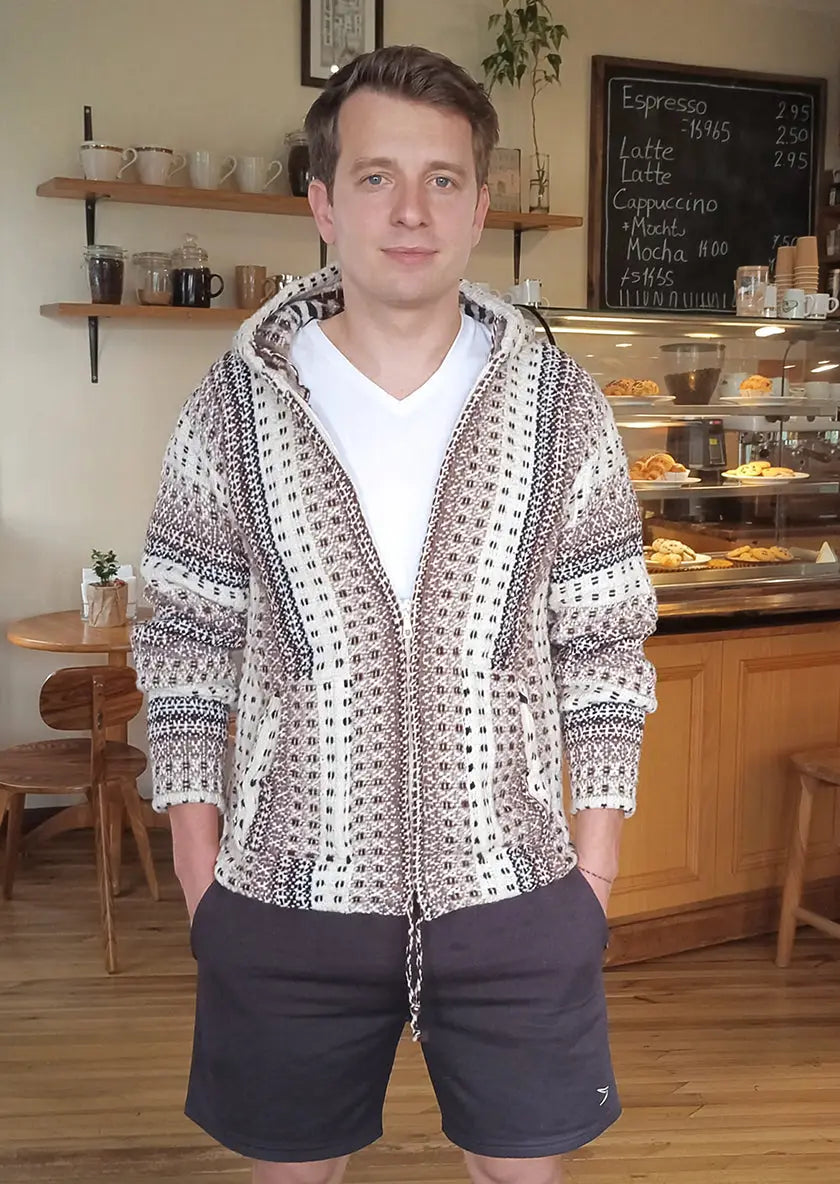 A man wearing a cream beige taupe and charcoal hand-knitted zip-up hoodie cardigan made of 100% sheep wool