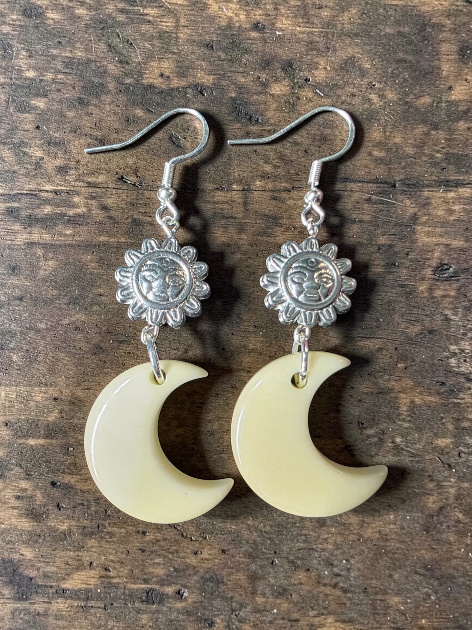 Moon-shaped earrings with sun designs on a wooden surface