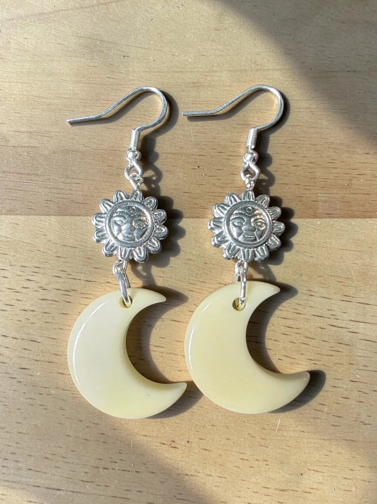 Silver sun-shaped charms hang above creamy off-white crescent moon carved tagua nut earrings lightweight from rainforest