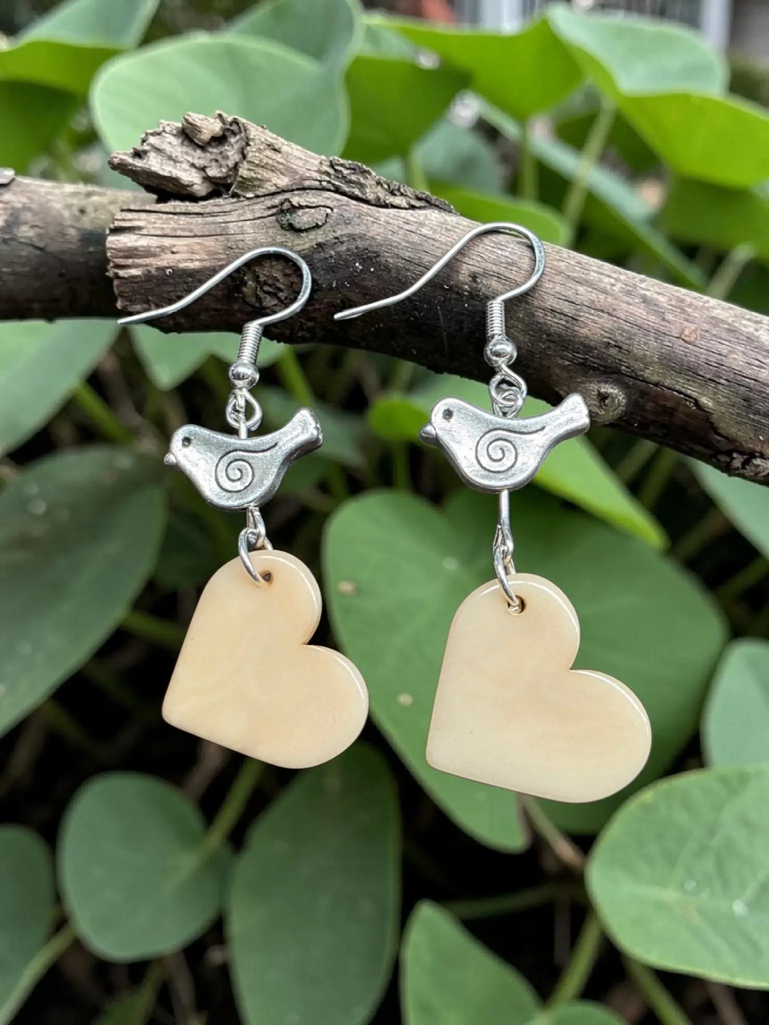 Silver bird-shaped earrings with cream tagua heart pendants carved from vegetable ivory from the rainforest