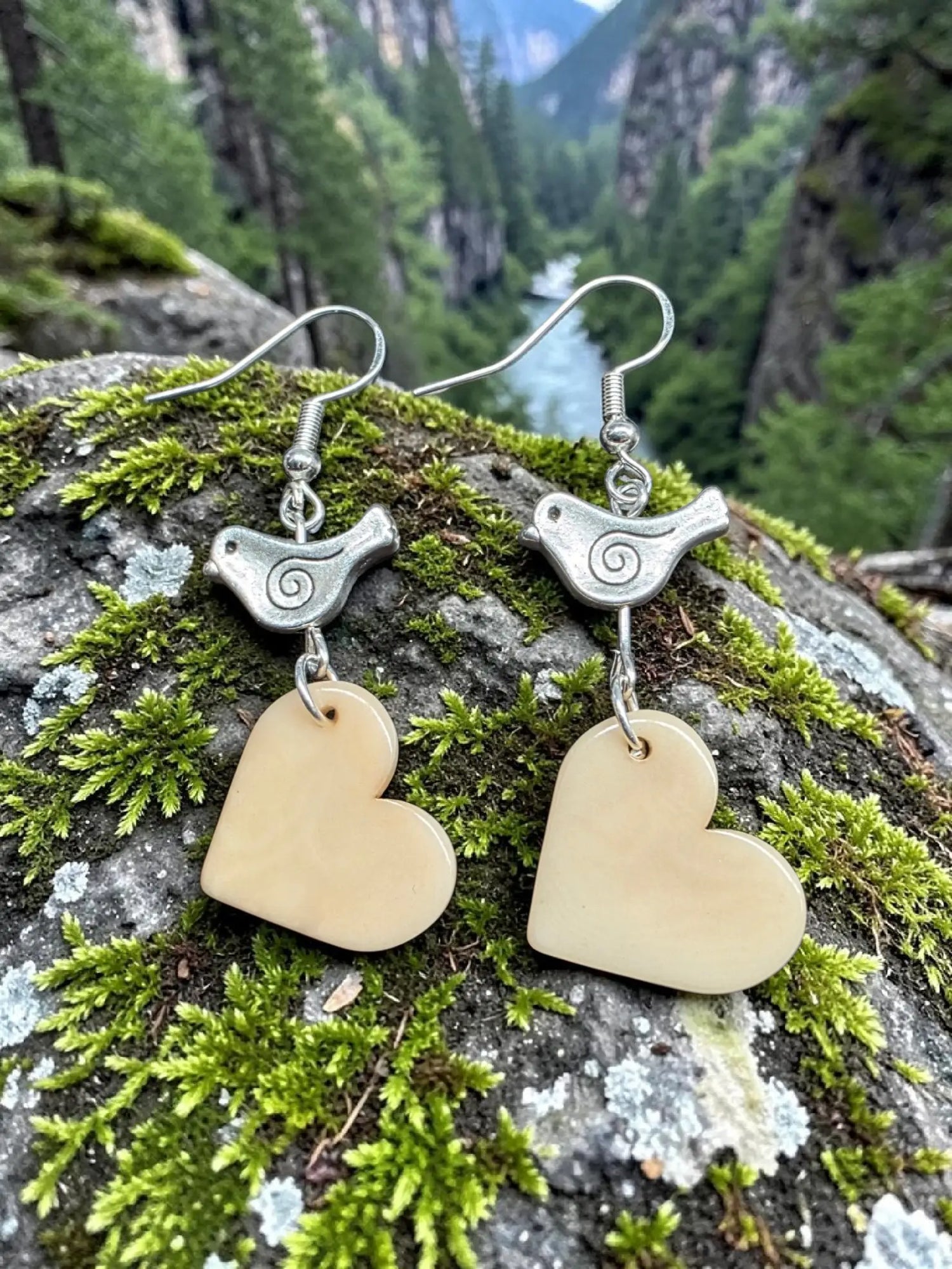 Silver bird-shaped earrings with spiral details and light beige carved vegetable ivory heart pendants from the rainforest
