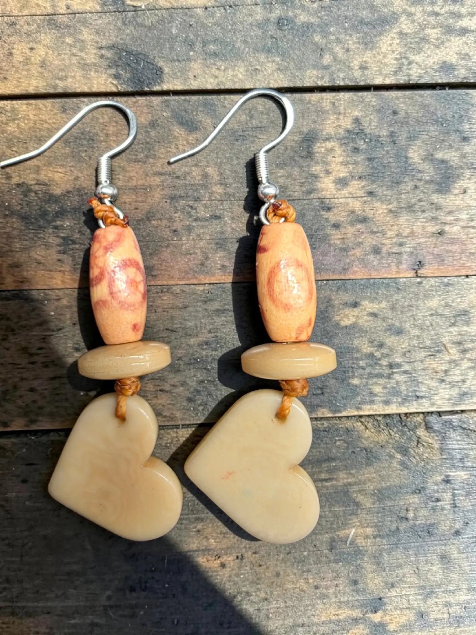 Cream tagua heart carved vegetable ivory earrings in beige with smooth stone-like texture and wooden bead detail