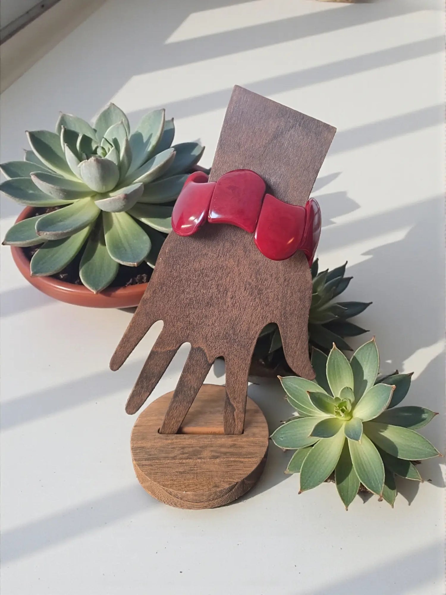 A vibrant dark red carved tagua nut bracelet with glossy finish displayed on wooden hand stand forest seed bracelets