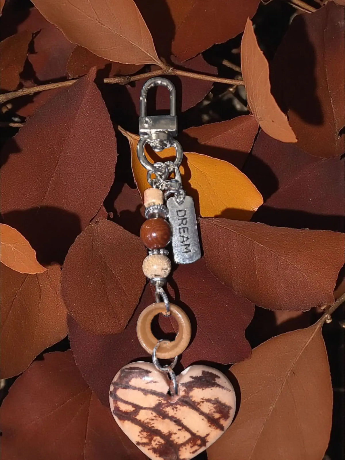Heart-shaped bag charm with natural carved marble tagua in beige and brown finish featuring wooden beads and silver dream tag