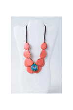 Coral-colored oval wooden pendant with blue bead in ella layered tagua slice necklace perfect layered tagua slice accessory
