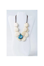 Cream-colored oval beads layered tagua slice necklace with blue pendant on adjustable dark brown cord