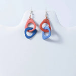 A pair of fern interlocking tagua earrings with peach and blue abstract circles and silver hooks