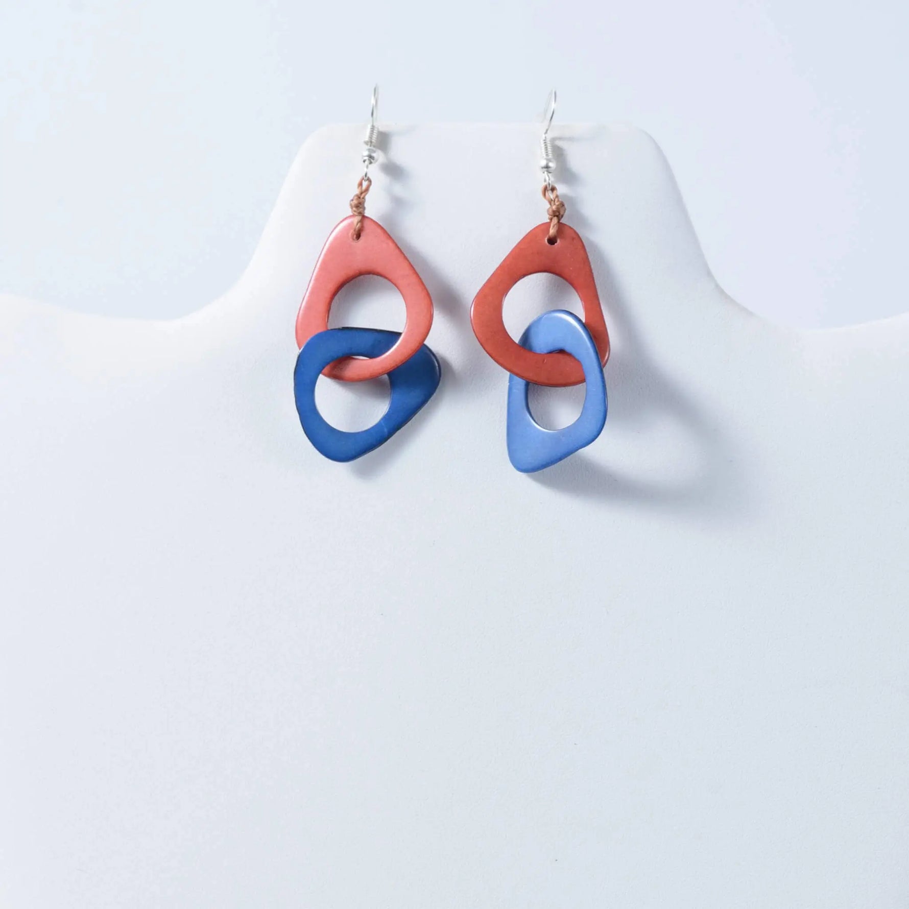 A pair of fern interlocking tagua earrings with peach and blue abstract circles and silver hooks