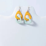 A pair of fern interlocking tagua earrings with bold yellow and soft mint green resin teardrop shapes