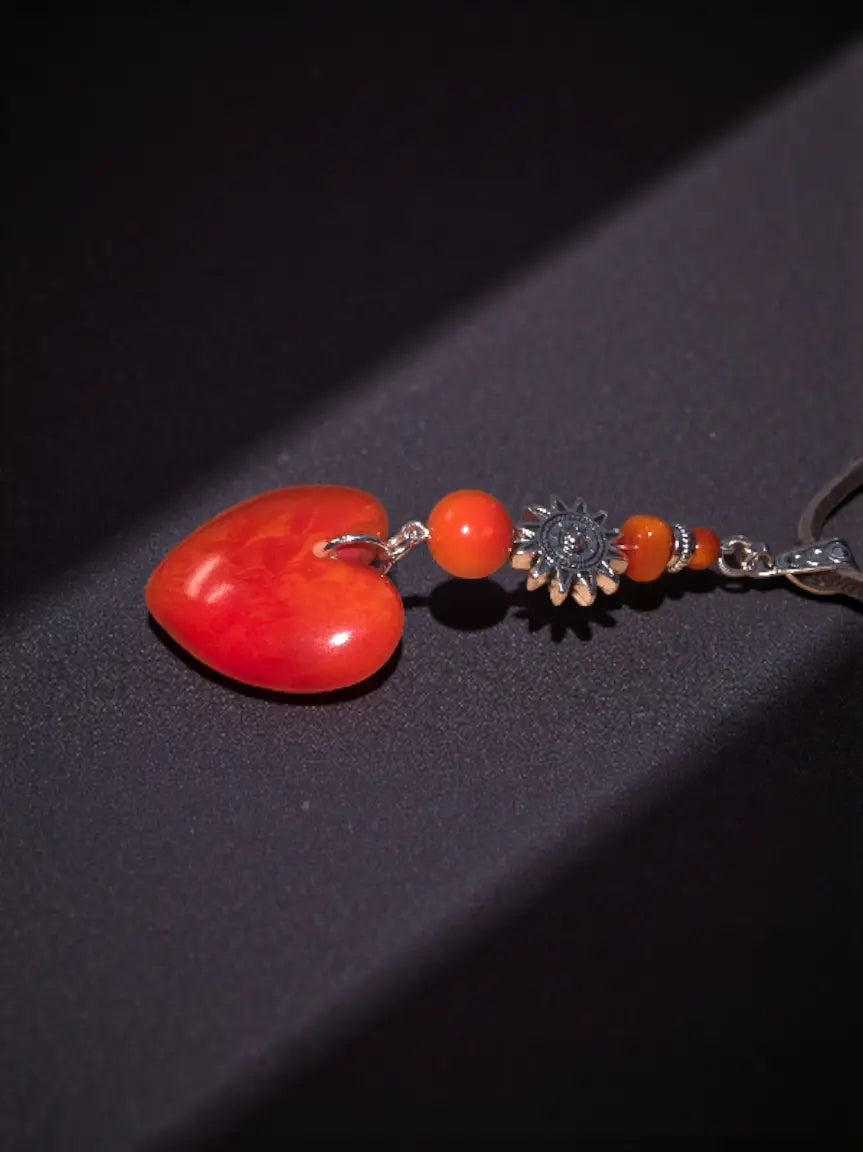 A vibrant red carved heart meets sun amulet pendant necklace with orange beads on an ornate silver-toned chain