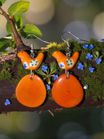 Folk art orange bird ceramic tagua slice earrings with green and blue floral patterns dangling from silver hooks