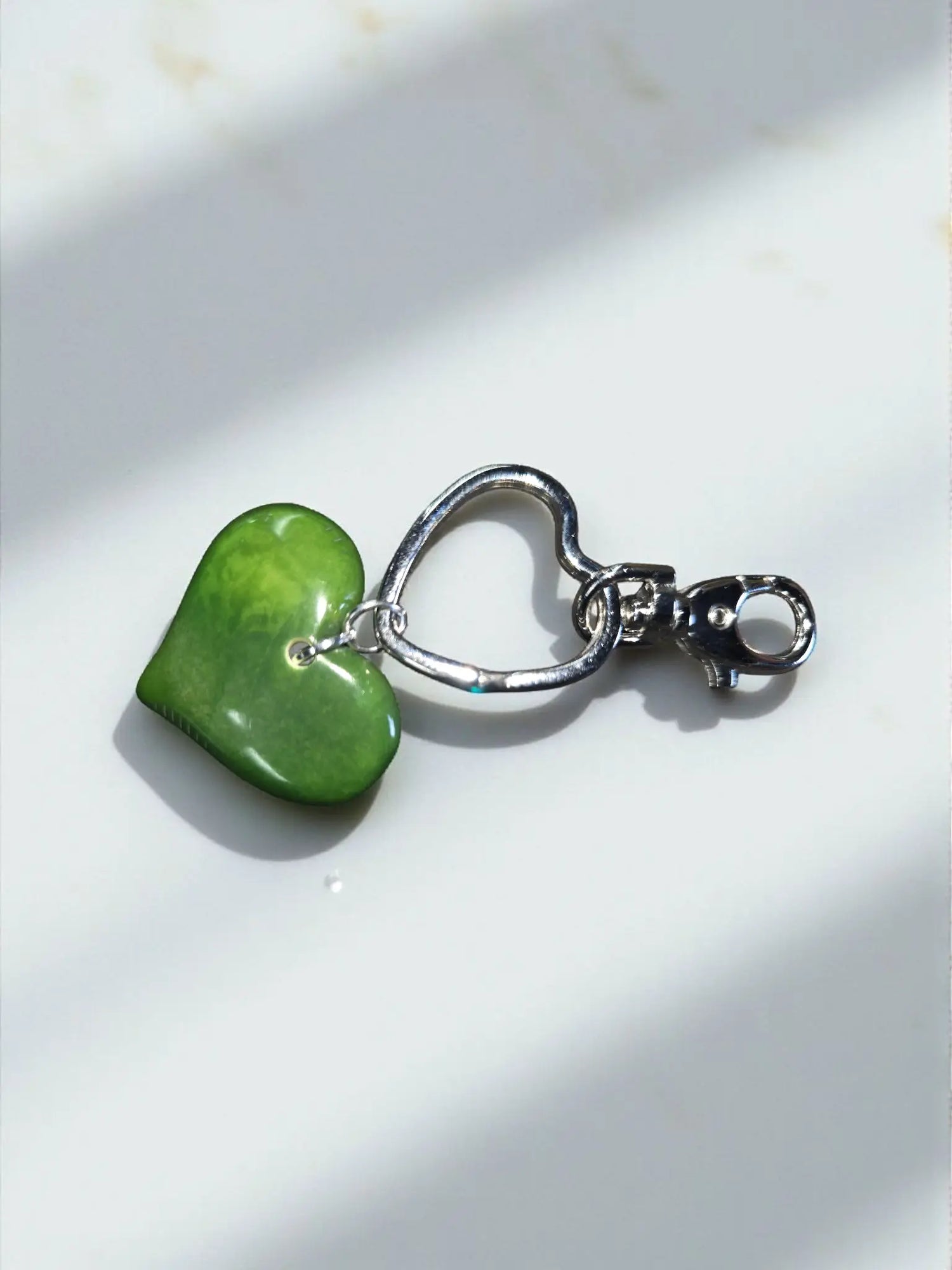 A smooth vibrant green heart-shaped polished stone pendant attached to a silver keychain bag charm