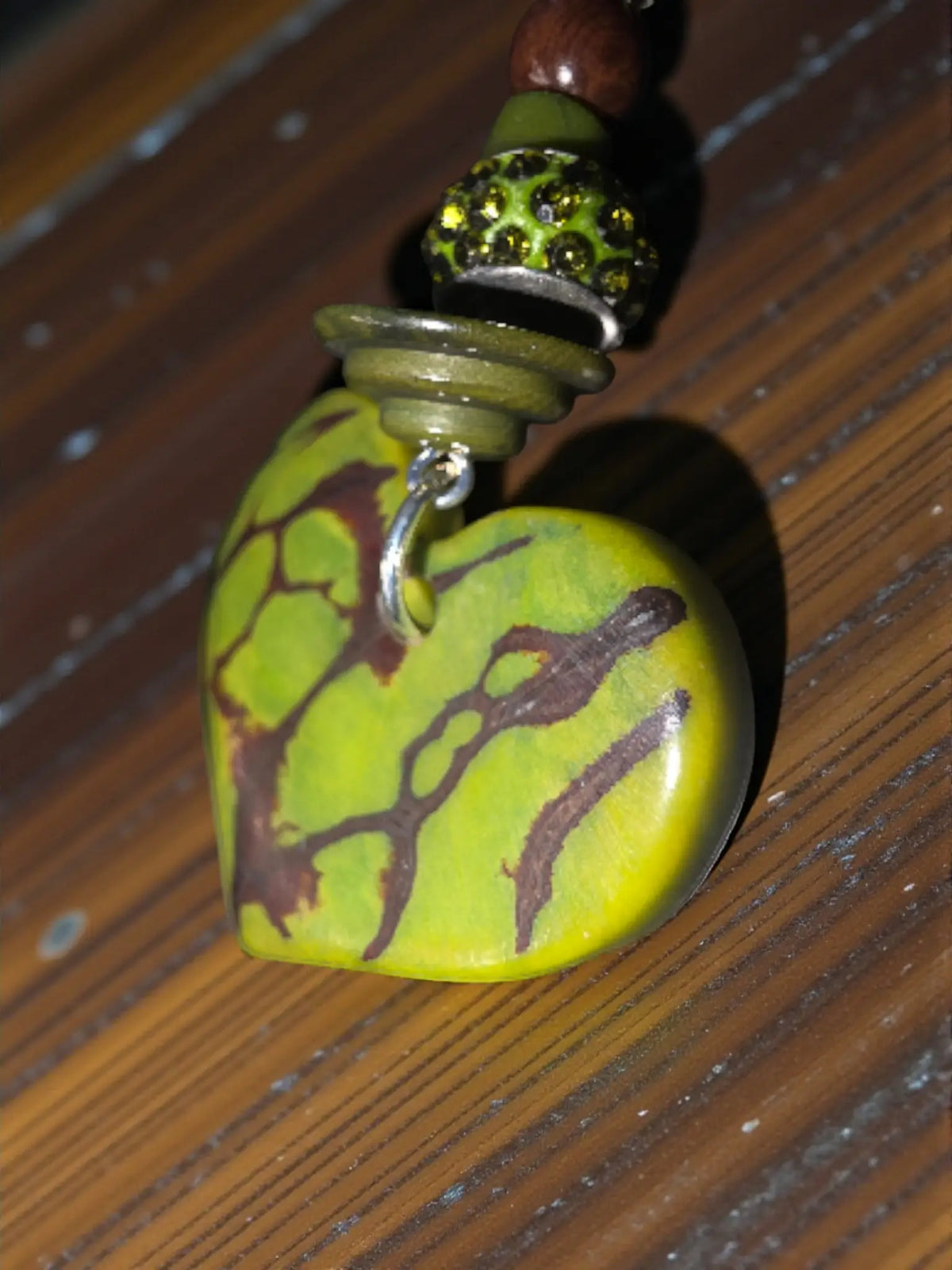 A vibrant lime green rustic carved tagua heart pendant necklace with marbled brown pattern and silver bail