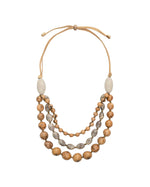 A layered idra necklace with natural wooden beads, silver-patterned discs, and beige leather cords featuring bombona seeds