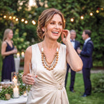 A woman wears a cream satin dress with a gold belt buckle paired with an idra necklace featuring bombona seeds
