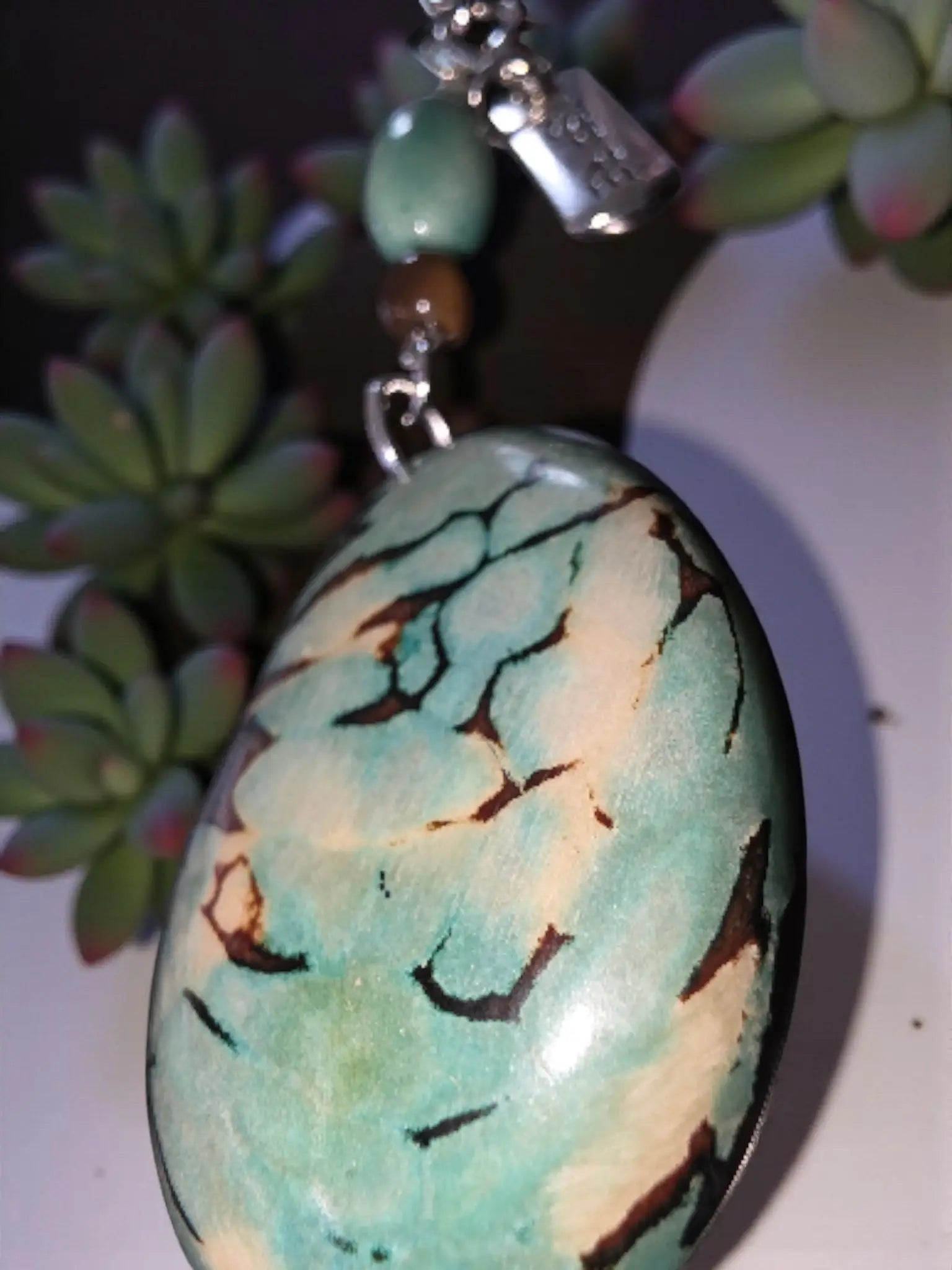 A polished oval turquoise stone pendant with teal cream and dark brown veins in inspire marble aqua tagua bag charm