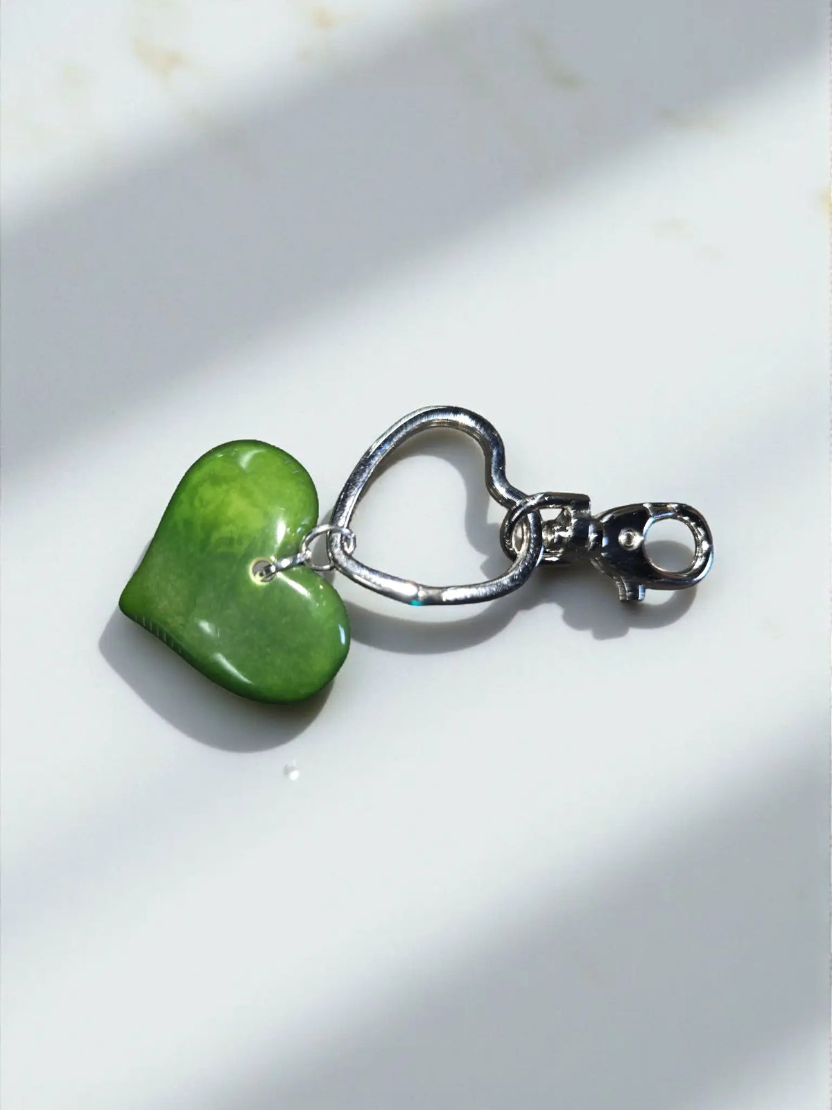 A smooth vibrant green heart-shaped polished stone pendant on a silver keychain bag charm with clasp