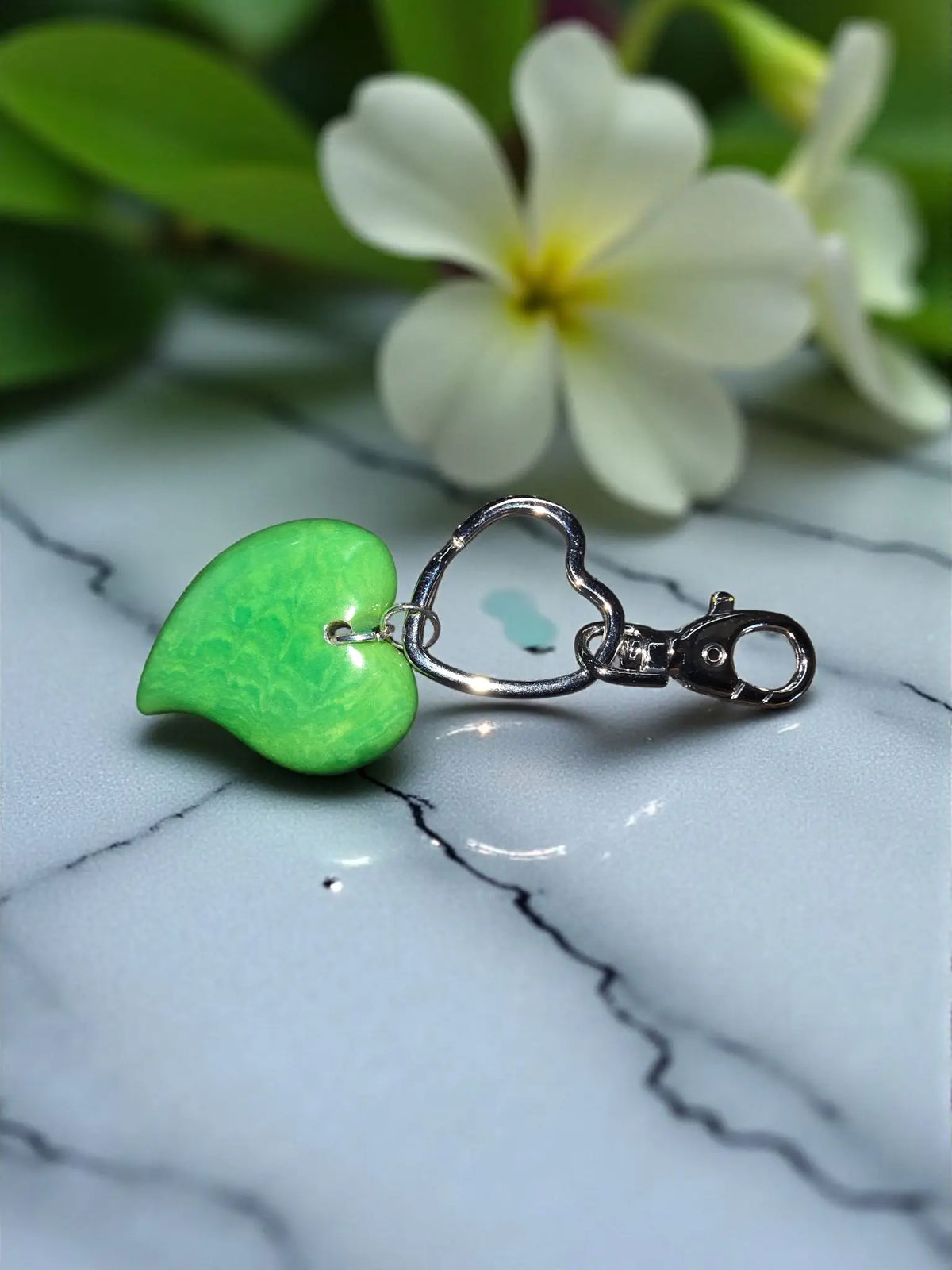 A kelly green heart keychain with a glossy finish and silver metal clasp used as a stylish bag charm
