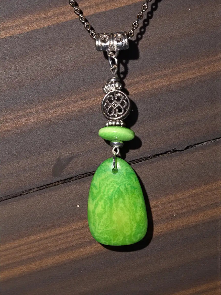A vibrant green teardrop tagua pendant with marbled texture hangs from an ornate silver-toned chain with beads