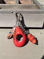 Vibrant red glossy large carved tagua bag charm with orange feather and translucent bead keychain accessory