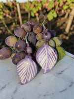 Sun & Wing Studio lavender purple leaf earrings carved from eco-friendly tagua nut, displayed on fresh grapes.
