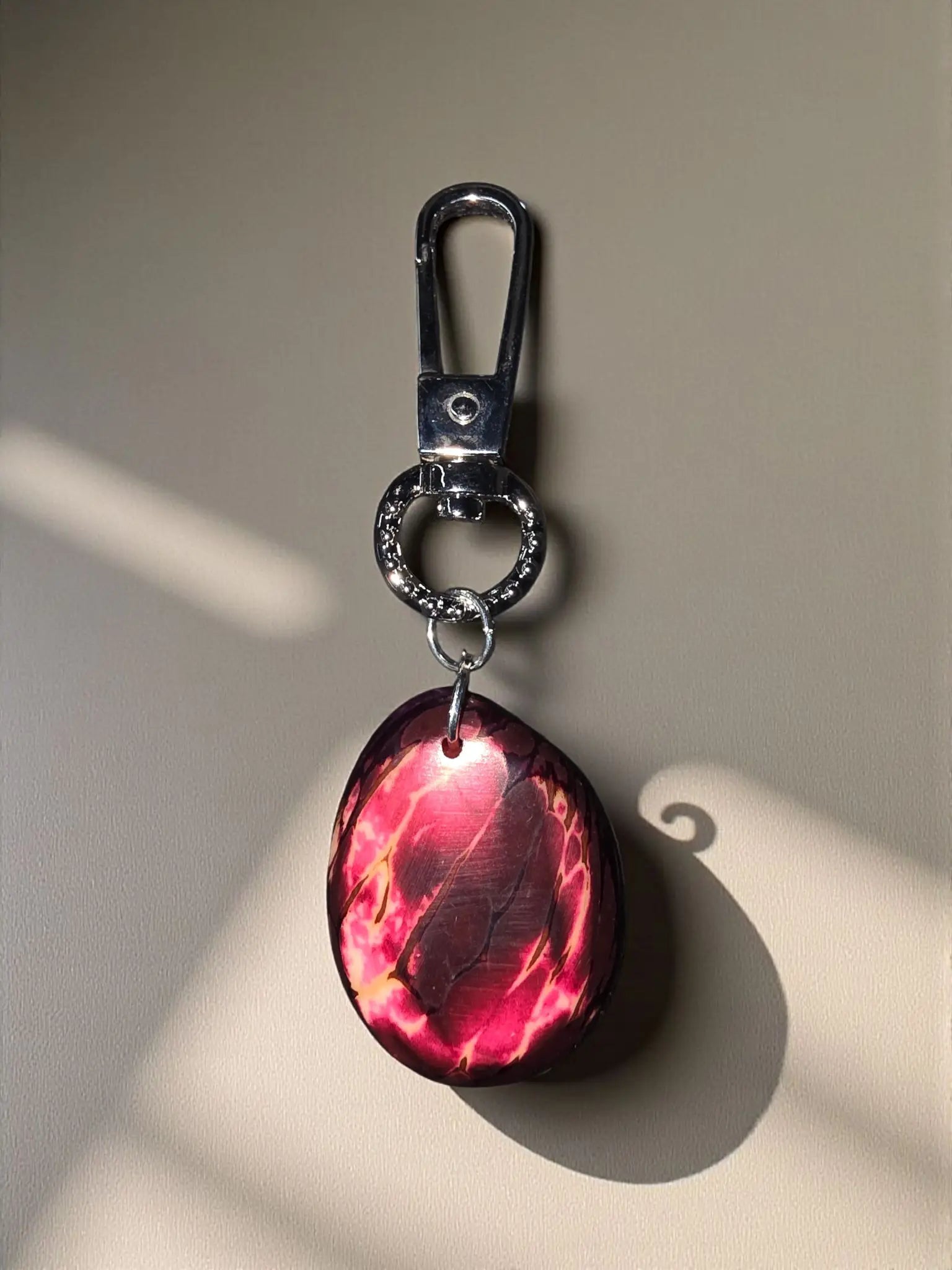 A glossy oval key chain bag charm with a red and pink marbled pattern and silver-toned metal clasp