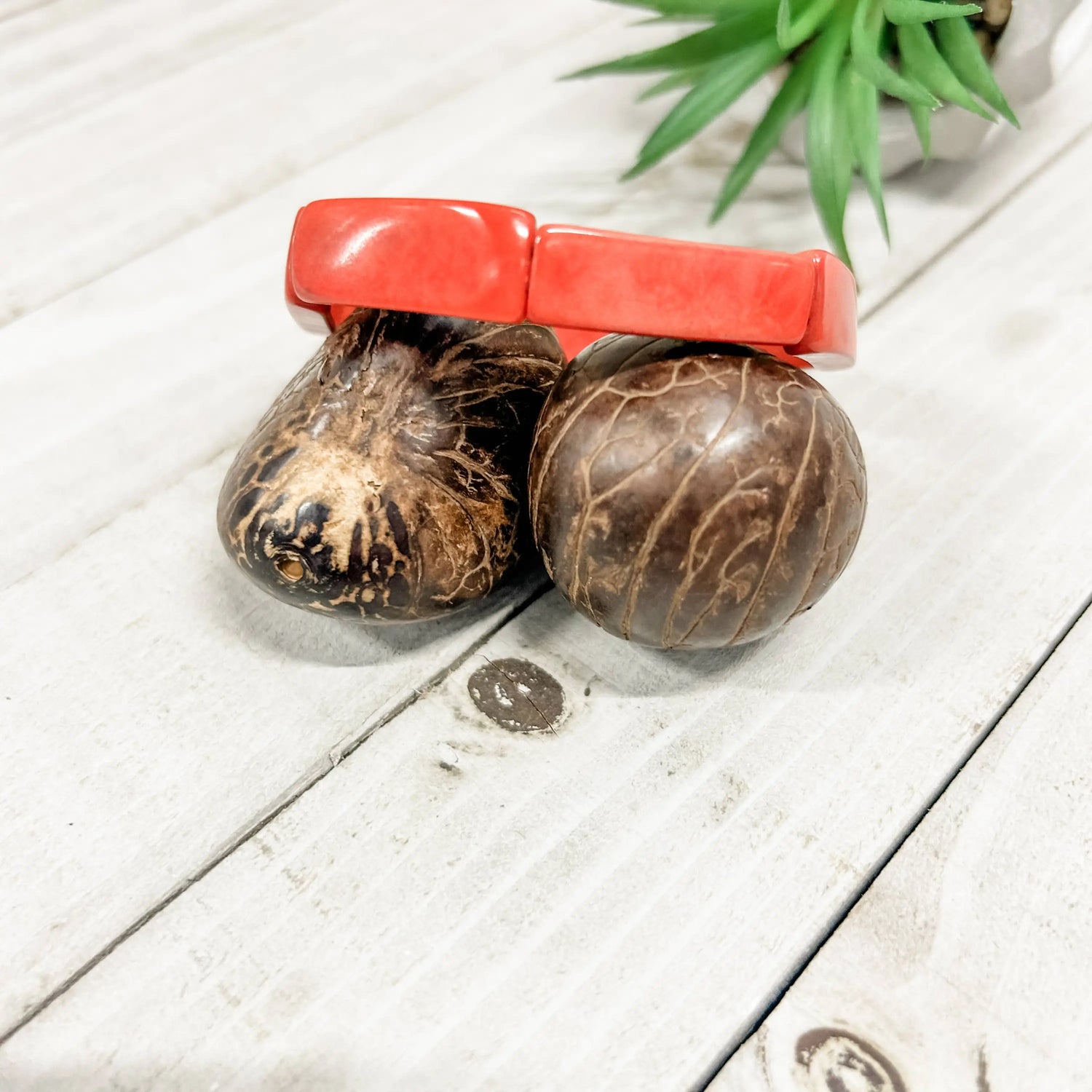 Loja bracelet coral with vibrant coral plastic clasp securing natural dark brown coconut shell maracas with textured ridges